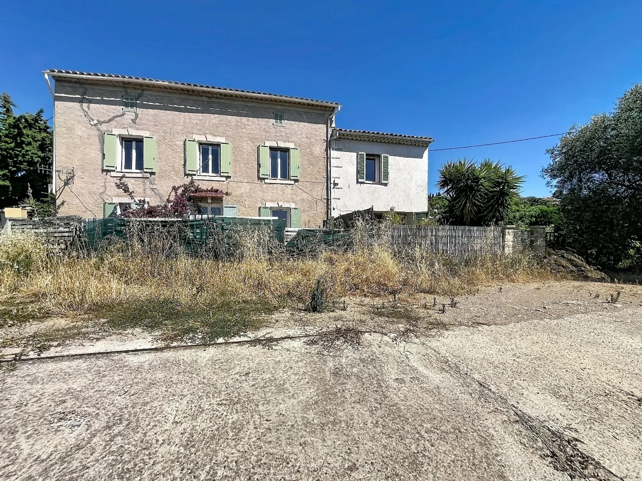 A real photo of the bastide: two levels, almond-green shutters, bougainvillea, a stone wall, an overgrown courtyard